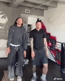Two Men Are Dancing In A Room With A Graffiti Wall Behind Them . GIF