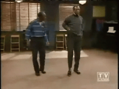 Two Men Are Dancing In A Room With A Tv Advertisement In The Corner GIF