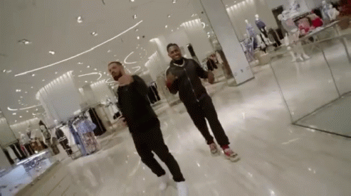 Two Men Are Dancing In A Shopping Mall While Looking At Clothes . GIF