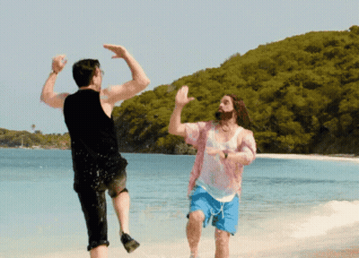 Two Men Are Dancing On A Beach And One Of Them Is Wearing A Pink Shirt And Blue Shorts GIF