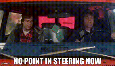 Two Men Are Driving A Red Van With The Words `` No Point In Steering Now '' On The Dashboard . GIF