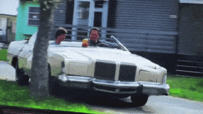Two Men Are Driving A White Car Down A Road GIF