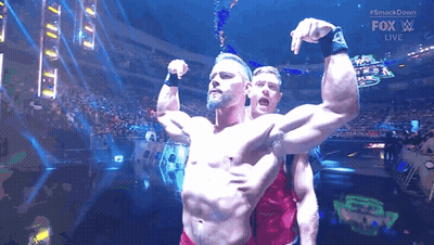 Two Men Are Flexing Their Muscles In Front Of A Crowd At A Wrestling Match . GIF