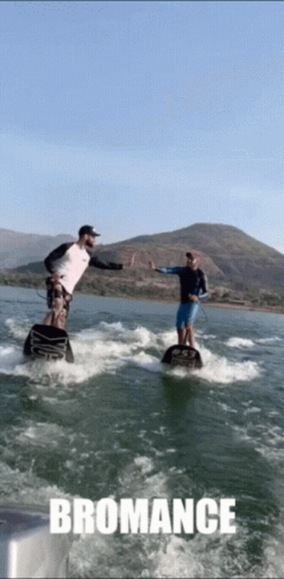Two Men Are Giving Each Other A High Five While Riding A Wave On A Body Of Water With The Word Bromance Below Them GIF