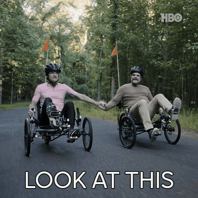 Two Men Are Holding Hands While Riding Three Wheeled Bicycles With The Words Look At This Below Them GIF