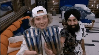 Two Men Are Holding Up Glasses In A Living Room GIF