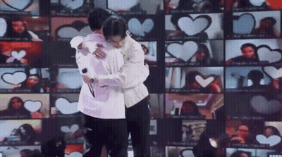Two Men Are Hugging Each Other In Front Of A Wall Of Hearts . GIF
