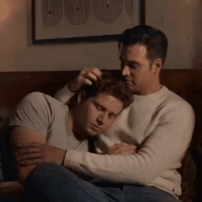 Two Men Are Hugging Each Other On A Couch In A Living Room . GIF