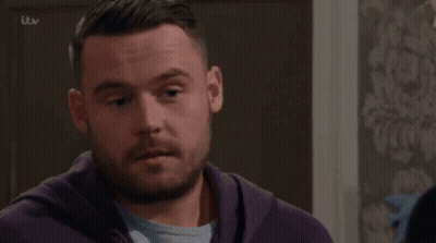 Two Men Are Kissing In Front Of A Cabinet With A Tv Logo On The Bottom Right GIF