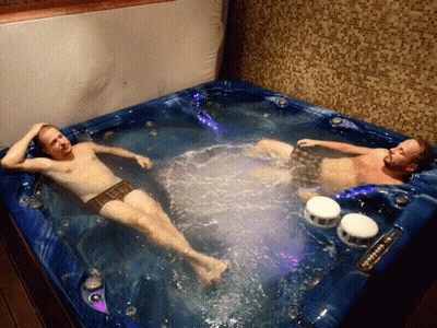 Two Men Are Laying In A Blue Hot Tub With A Purple Light GIF