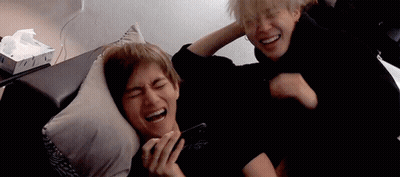 Two Men Are Laying On A Couch And Laughing While One Of Them Is Holding A Cell Phone . GIF