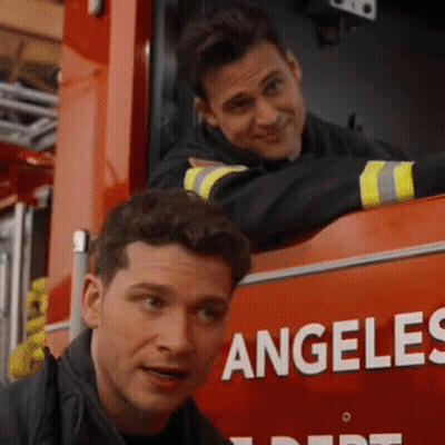 Two Men Are Leaning On The Side Of A Fire Truck That Says Angeles GIF