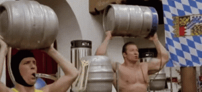 Two Men Are Lifting Kegs Over Their Heads In Front Of A Flag GIF