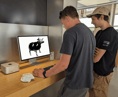 Two Men Are Looking At A Computer Monitor With A Cow On It GIF
