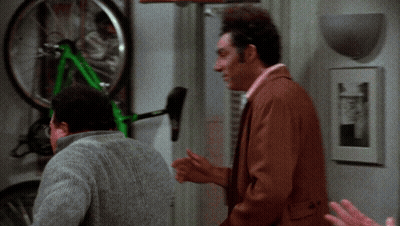 Two Men Are Looking At A Green Bicycle That Is Hanging On A Wall GIF