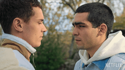 Two Men Are Looking At Each Other And One Has A Netflix Logo On His Shirt GIF