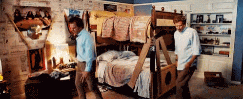 Two Men Are Moving A Bunk Bed In A Room With Posters On The Wall GIF