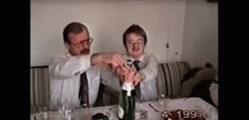 Two Men Are Opening A Bottle Of Champagne Together . GIF