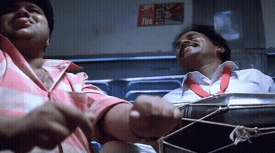 Two Men Are Playing A Drum In Front Of A Fire Sign GIF