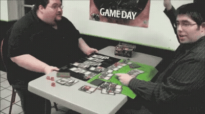 Two Men Are Playing A Game At A Table In Front Of A Game Day Poster . GIF