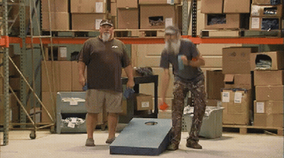 Two Men Are Playing A Game In A Warehouse With Boxes On The Shelves GIF