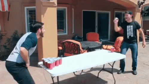 Two Men Are Playing A Game Of Beer Pong On A Table With Red Cups GIF