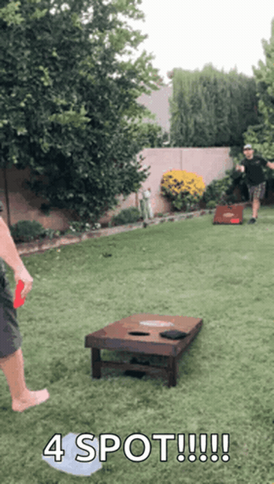 Two Men Are Playing A Game Of Cornhole In A Backyard And One Of Them Is Holding A Frisbee . GIF