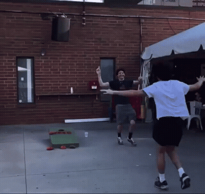 Two Men Are Playing A Game Of Cornhole In Front Of A Building GIF