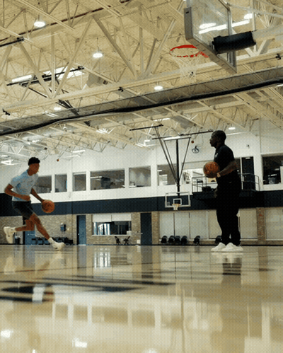 Two Men Are Playing Basketball In A Gym With A Hoop In The Background GIF