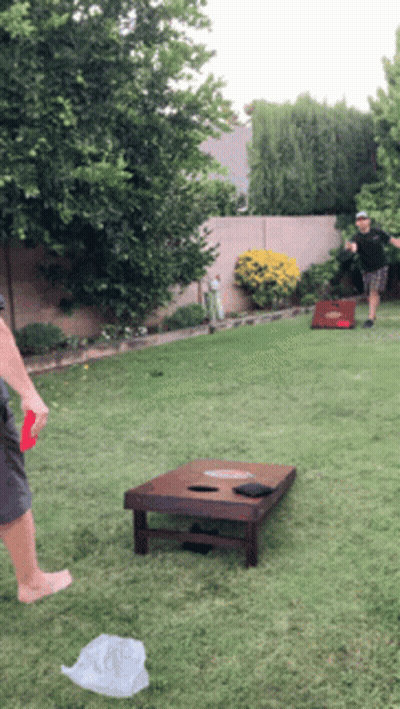 Two Men Are Playing Cornhole In The Backyard GIF