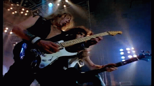 Two Men Are Playing Guitars On A Stage And One Of Them Is Wearing A Black Vest GIF