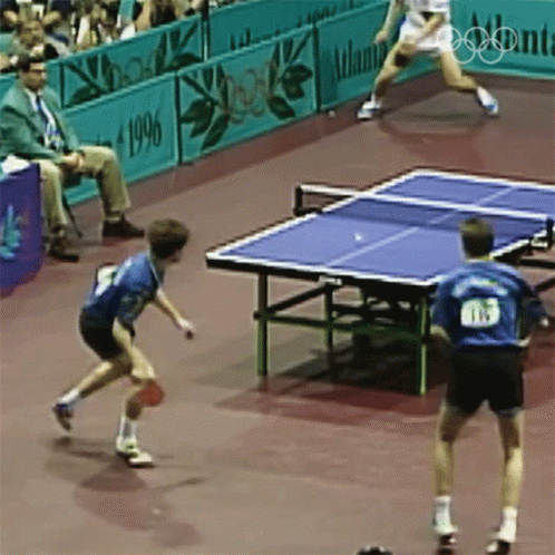 Two Men Are Playing Ping Pong In Front Of A Sign That Says Atlanta GIF