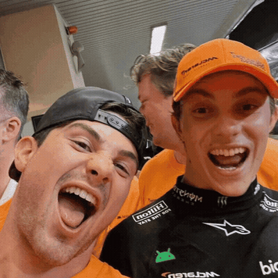 Two Men Are Posing For A Picture With One Wearing An Orange Hat That Says ' Triumph ' On It GIF