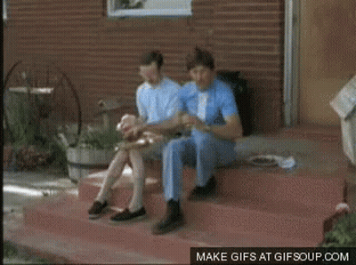 Two Men Are Riding A Bicycle On A Dirt Road With Mountains In The Background GIF