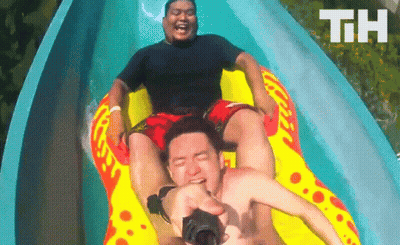 Two Men Are Riding Down A Water Slide With The Letters Th Visible In The Background GIF