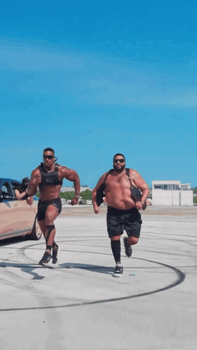 Two Men Are Running In A Parking Lot With One Wearing A Weighted Vest GIF