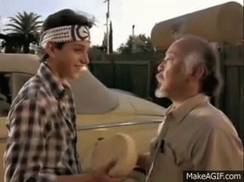Two Men Are Shaking Hands In Front Of A Car In A Movie . GIF