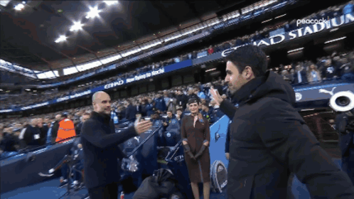 Two Men Are Shaking Hands In Front Of A Peacock Stadium Banner GIF