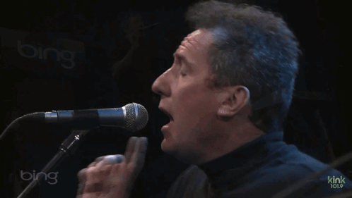 Two Men Are Singing And Playing Keyboards In Front Of A Bing Sign GIF
