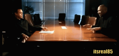 Two Men Are Sitting At A Conference Table With The Hashtag Itsreal85 GIF