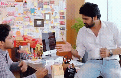Two Men Are Sitting At A Desk In Front Of A Computer And Talking . GIF
