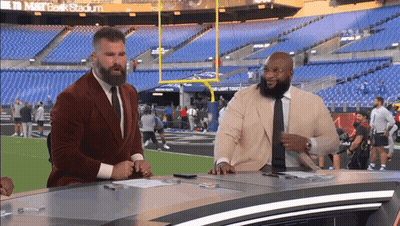 Two Men Are Sitting At A Desk In Front Of A Stadium That Says M & T Bank Stadium GIF