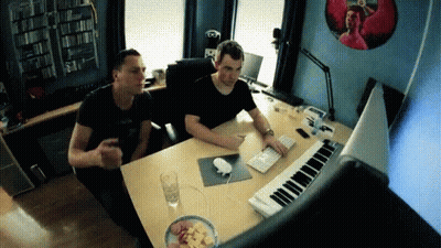 Two Men Are Sitting At A Desk With A Keyboard GIF