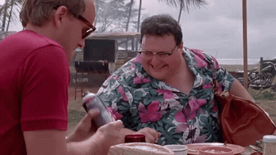 Two Men Are Sitting At A Table And One Is Holding A Can Of Soda GIF