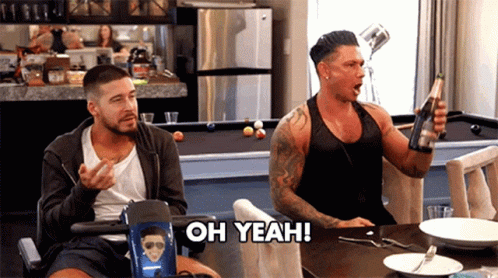 Two Men Are Sitting At A Table And One Of Them Is Holding A Bottle Of Champagne And The Other Is Saying Oh Yeah GIF