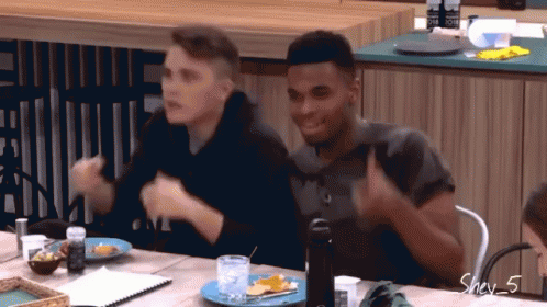 Two Men Are Sitting At A Table And One Of Them Is Wearing A Shirt That Says One On It GIF