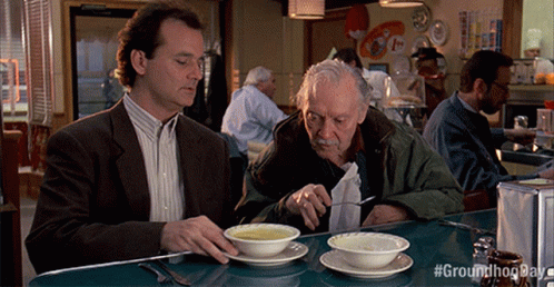Two Men Are Sitting At A Table Eating Soup With #Groundhogday Written On The Bottom Right GIF