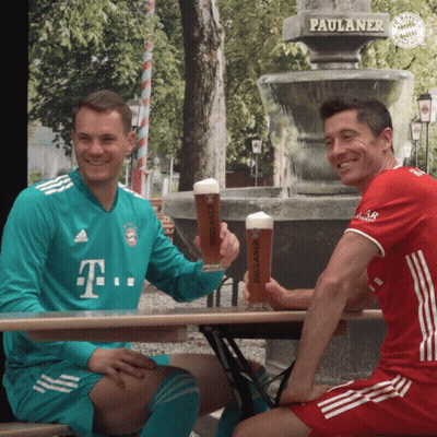 Two Men Are Sitting At A Table Holding Paulaner Beer GIF