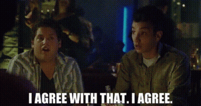 Two Men Are Sitting At A Table In A Bar And Talking To Each Other . GIF