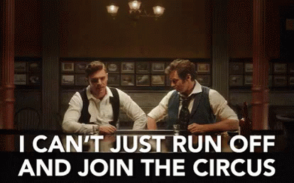 Two Men Are Sitting At A Table In A Dark Room Talking To Each Other . GIF